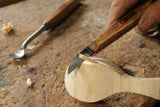 Straight carving knife being used to carve side of wooden spoon